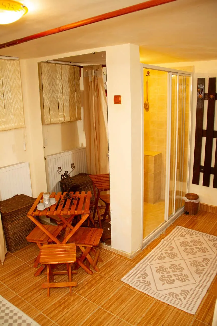 Cozy corner with a small wooden folding table and four matching stools on tiled floor, near a glass shower enclosure and a beige patterned rug.